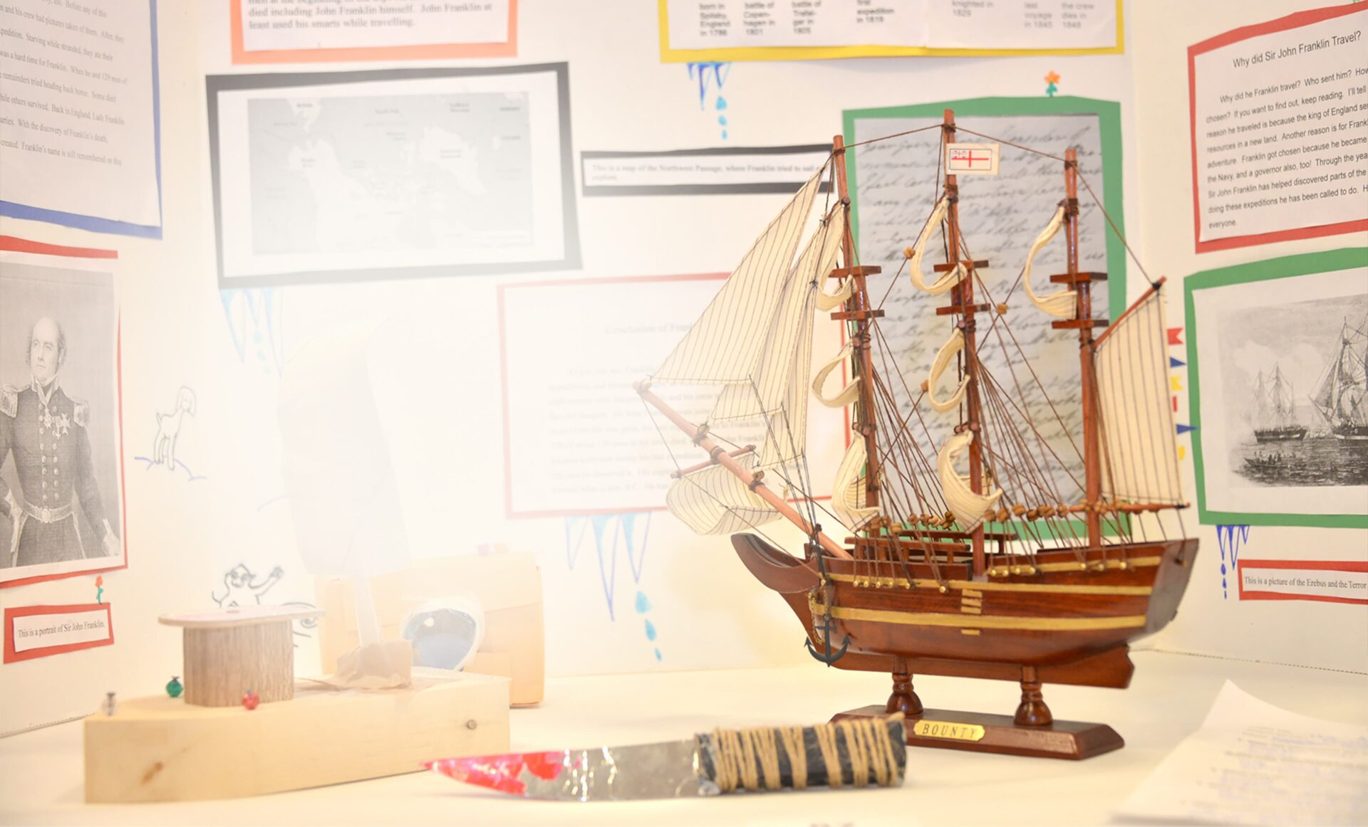 Photo showing a model ship, picture of a soldier on the left and picture of ships of the right