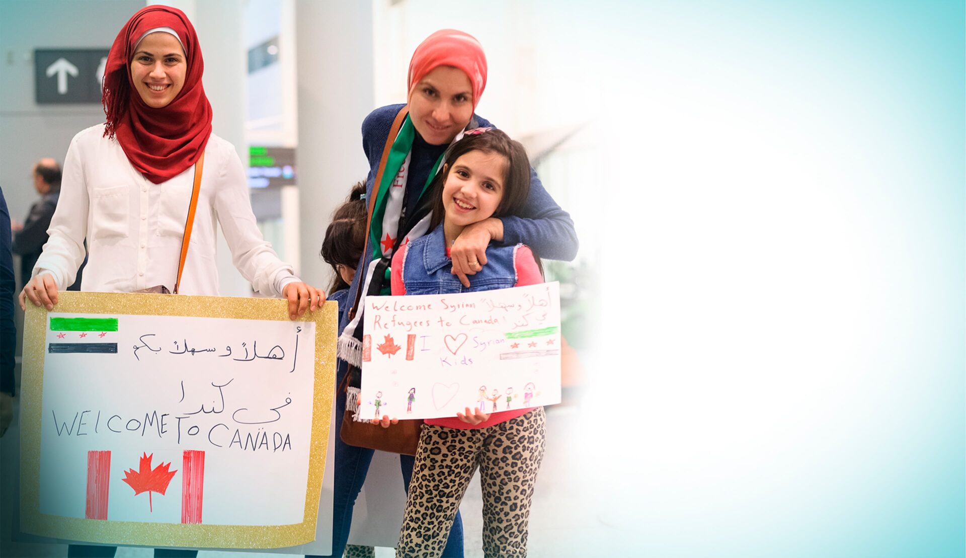Photo of two women and a young girl holding welcome to Canada boards for new immigrants