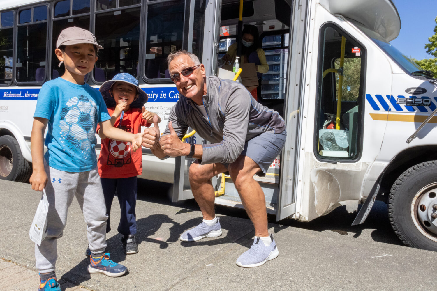 2 kids and a bus driver smiling posed in front of a bus.